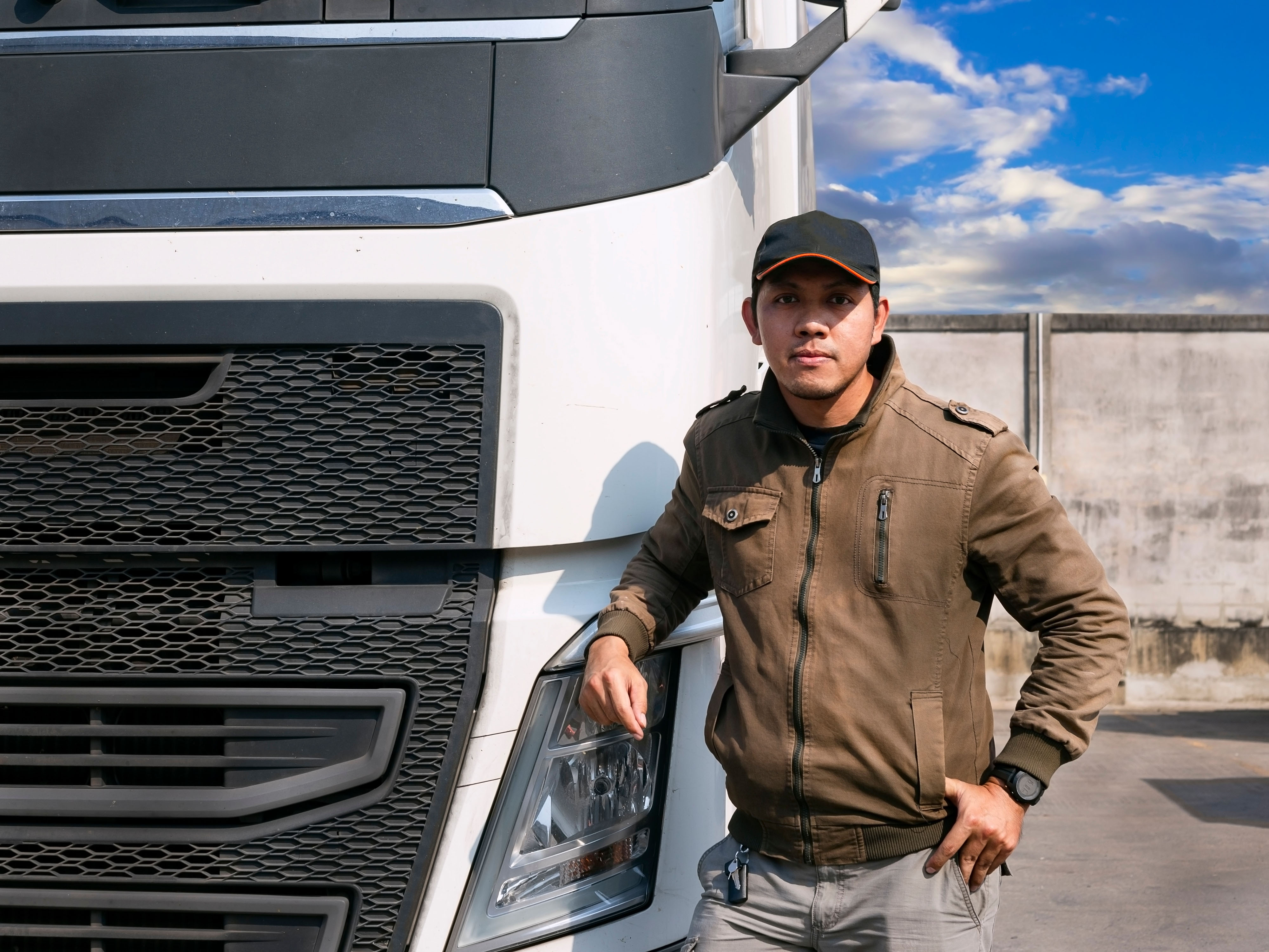 Professional truck driver standing beside a large commercial tractor-trailer, confident posture, industrial freight yard background