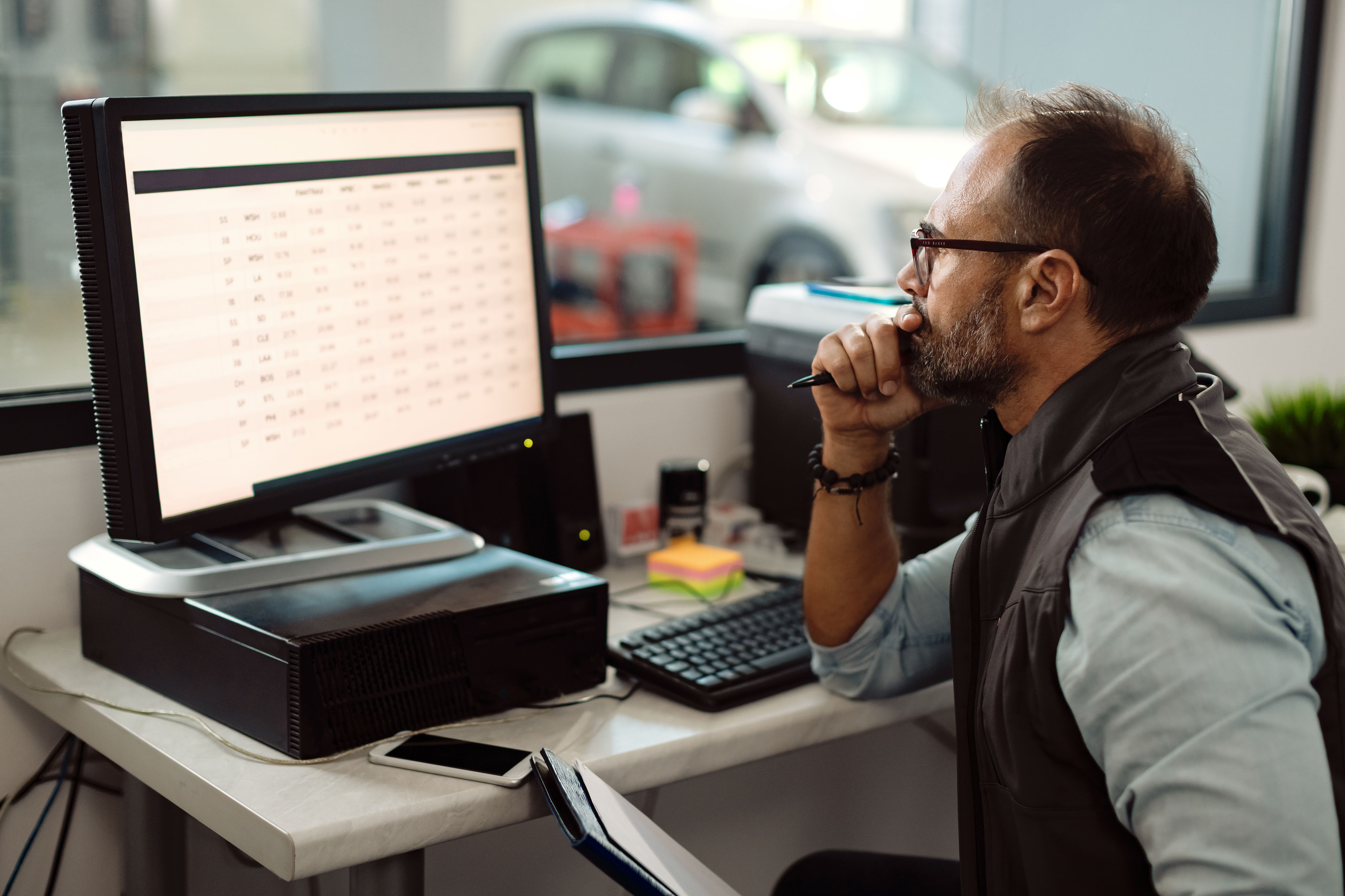 Freight analyst reviewing shipping invoice data on multiple monitors in a logistics operations center, focused and professional