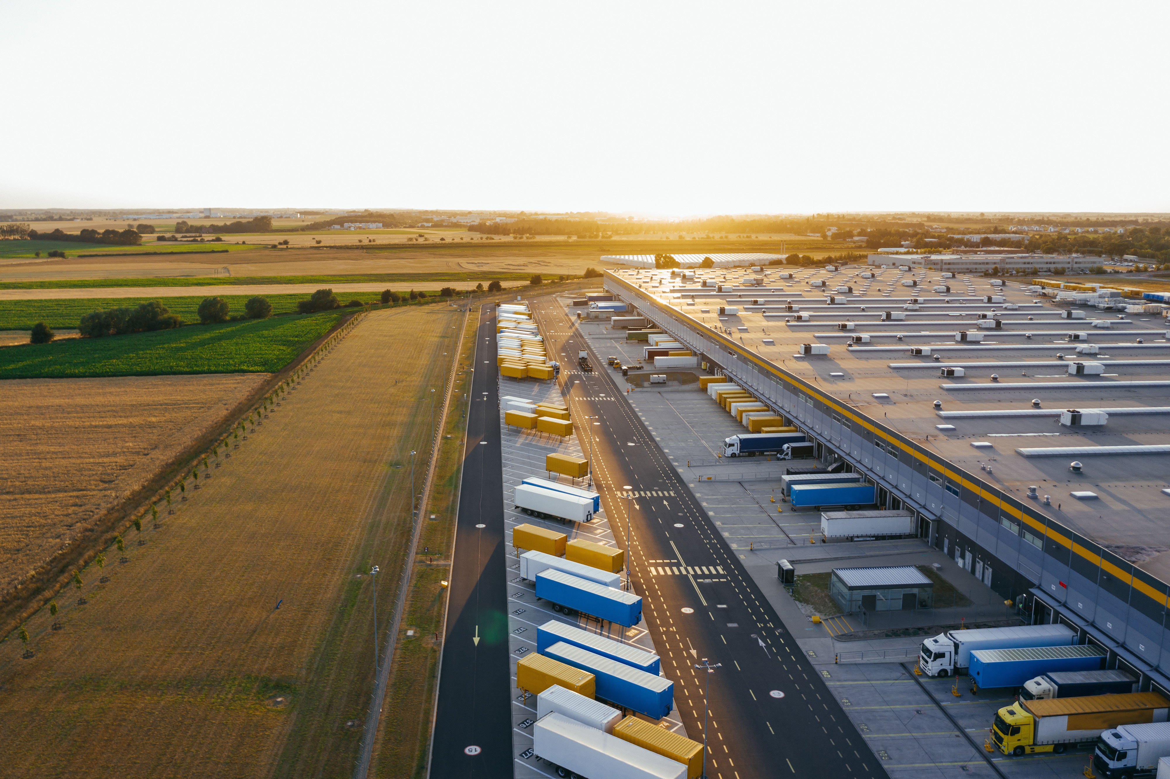 Aerial view of a major freight hub at dusk, rows of shipping containers and trucks under warm industrial lighting